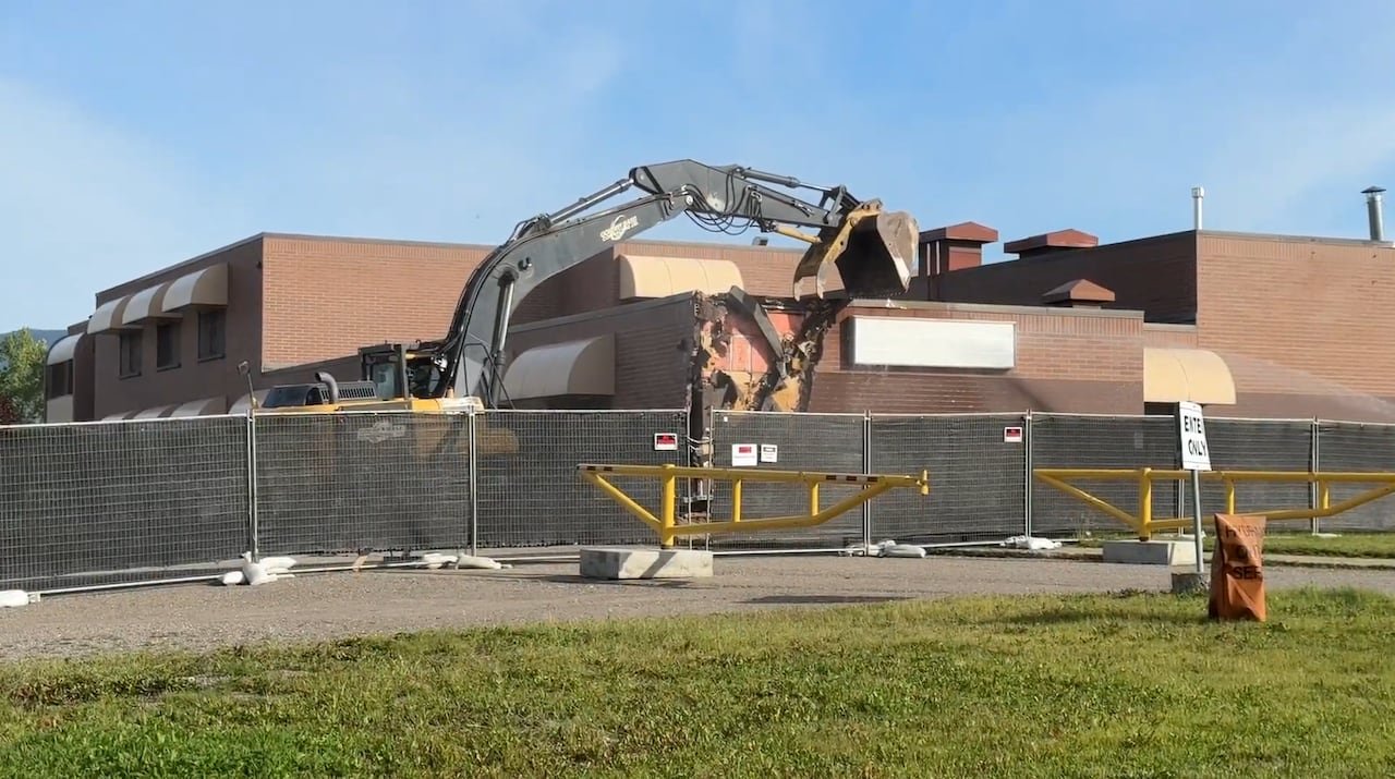 An excavator is pictured tearing down the corner of a building, exposing bricks on its corner.